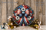 a decorative wreath with a patriotic design, including a large American flag ribbon and various flowers and foliage. The wreath is displayed on a wooden surface, surrounded by additional floral arrangements.