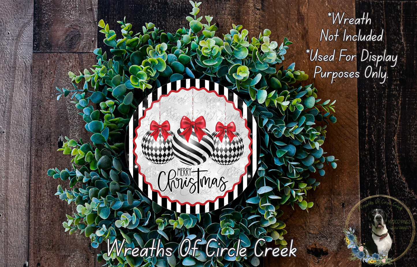 A Christmas wreath made of green leaves and two black and white ornaments with red bows, displayed on a wooden surface.