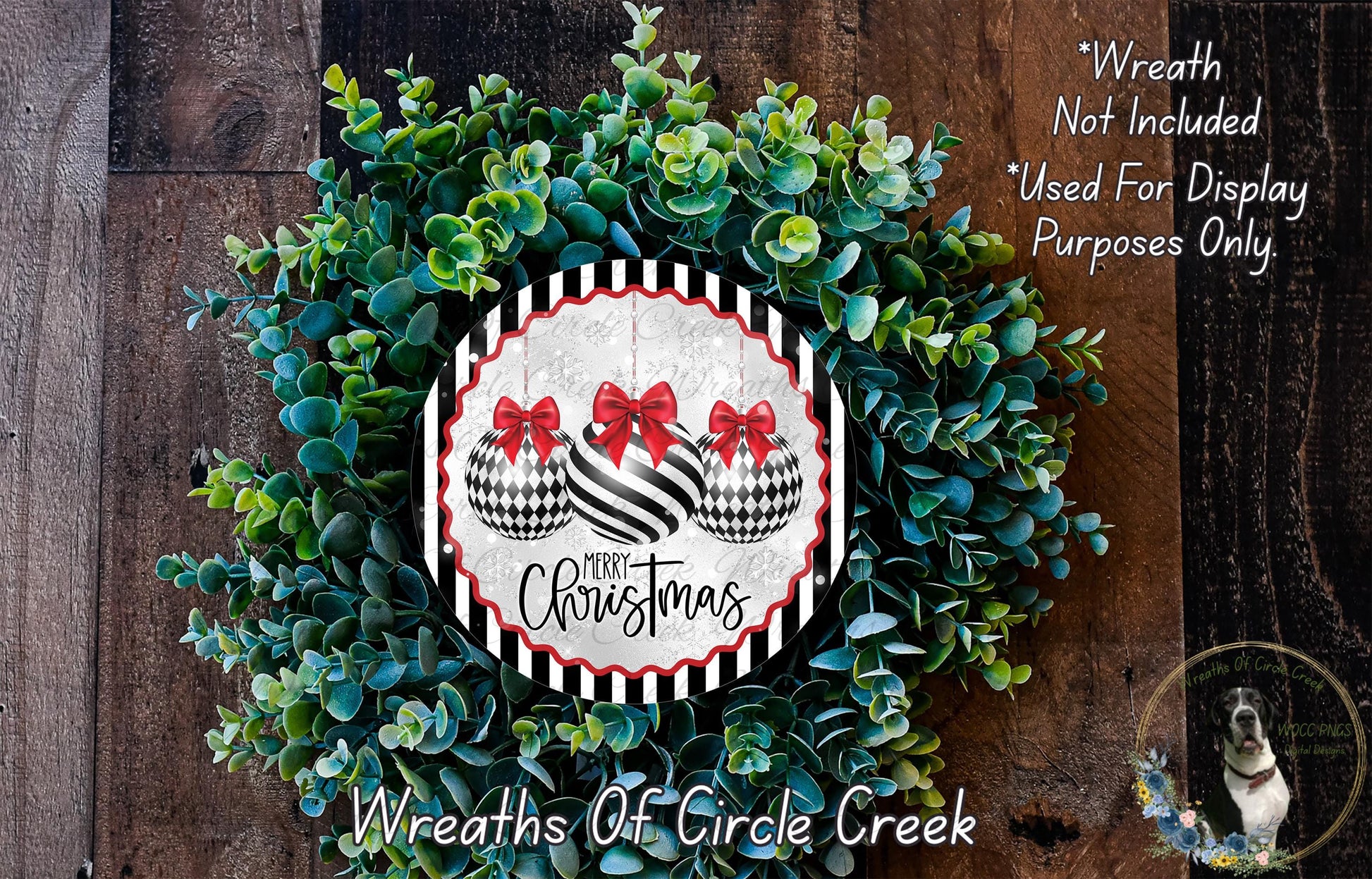 A Christmas wreath made of green leaves and two black and white ornaments with red bows, displayed on a wooden surface.