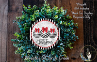 A Christmas wreath made of green leaves and two black and white ornaments with red bows, displayed on a wooden surface.