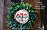 A Christmas wreath made of green leaves and two black and white ornaments with red bows, displayed on a wooden surface.