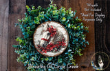 A wreath made of green leaves and a white horse with a red bow on its head, placed on a wooden surface.