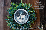 A wreath made of green leaves and a silver circular frame containing a photograph of two deer in a snowy forest.