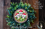 A wreath made of green foliage and featuring three penguins wearing Santa hats.