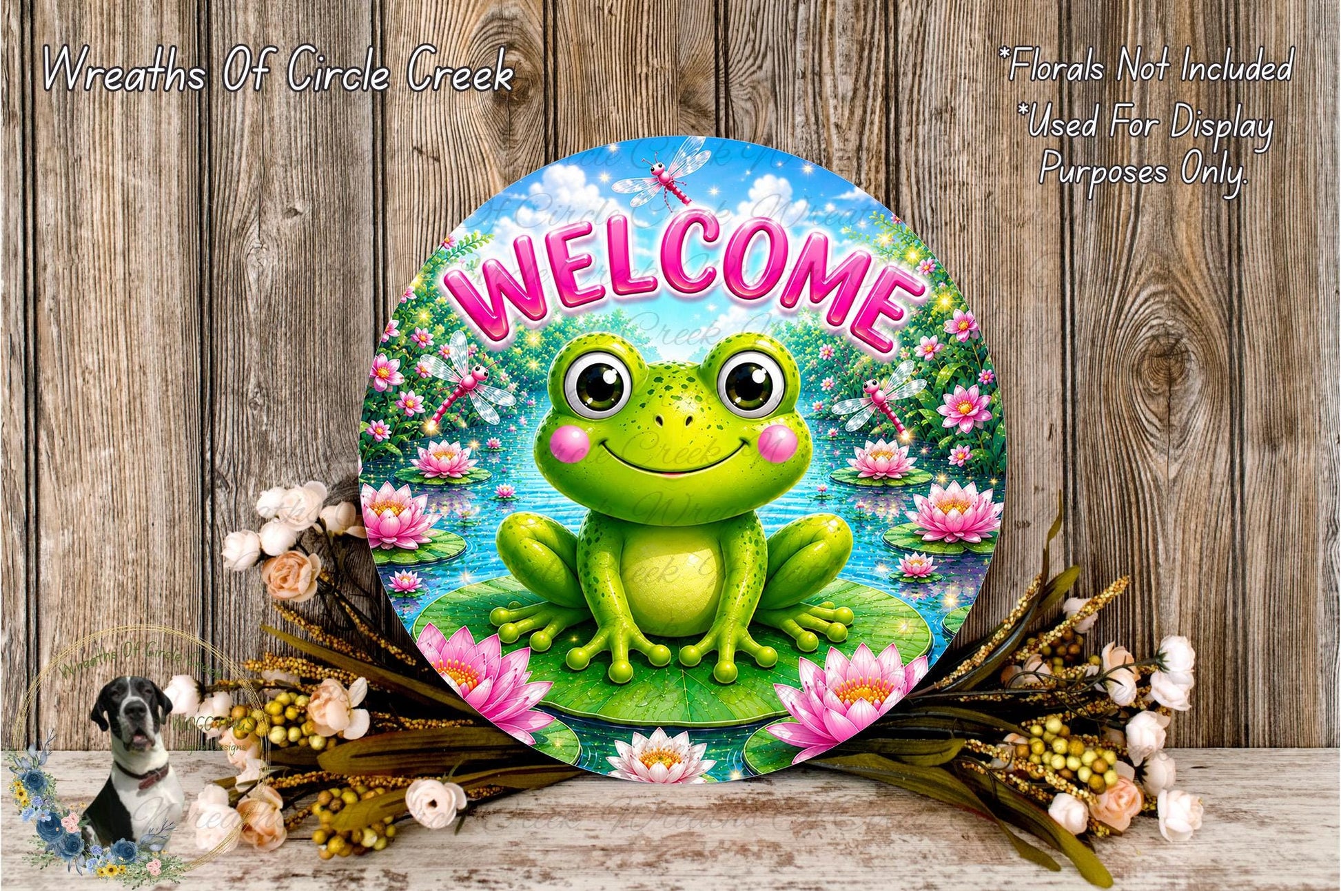 A round sign with a green frog sitting on a lily pad, surrounded by flowers and a wooden background.