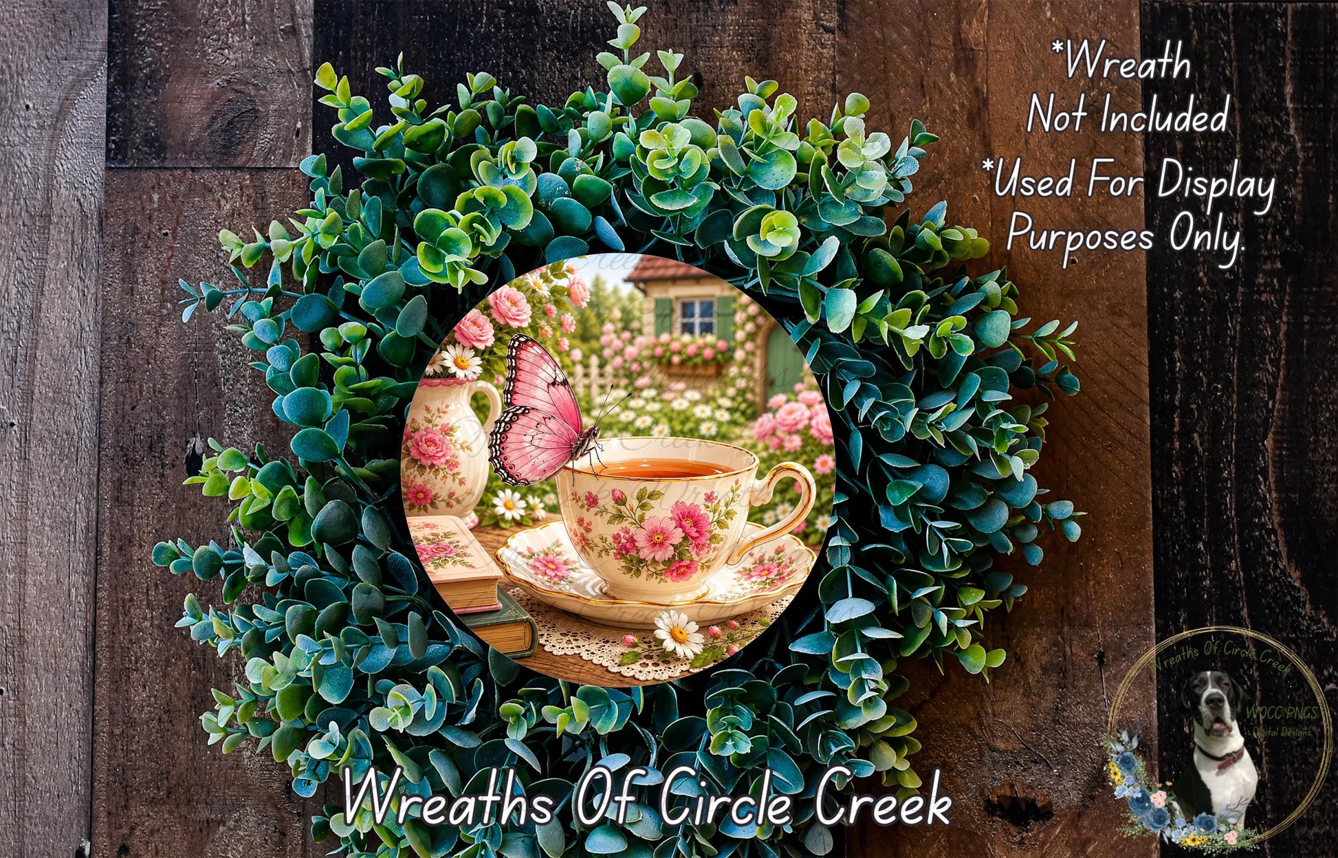 A wreath made of green leaves and flowers, with a teacup and a butterfly resting on it. The wreath is displayed on a wooden surface, and there is a small dog in the bottom right corner.