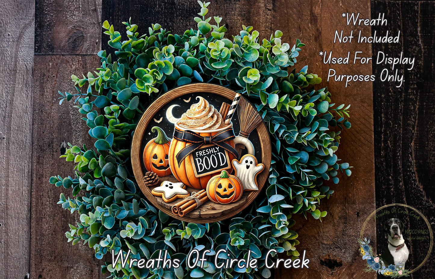 a Halloween-themed wreath made of green foliage and decorated with a pumpkin, ghost, and other spooky elements. The wreath is displayed on a wooden surface, and there is a small dog in the bottom right corner of the image.