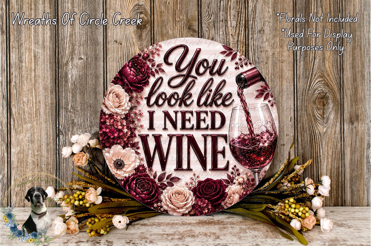 a decorative sign with the text "You look like I need wine" surrounded by a floral arrangement and a wine glass.