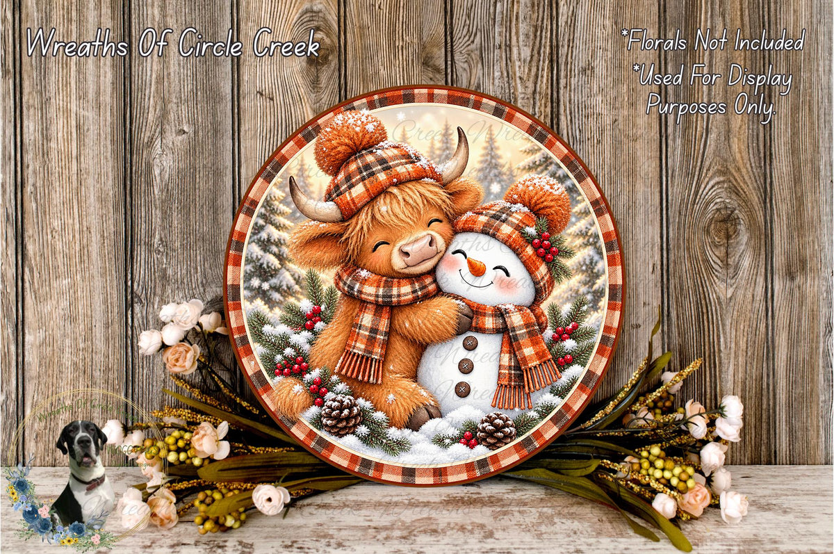 A decorative wreath featuring a snowman and a cow, surrounded by flowers and pine cones, against a wooden background.