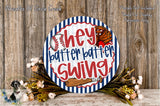 a round sign with the text "Hey batter, batter swing" and a baseball graphic, surrounded by a floral arrangement and a wooden background.