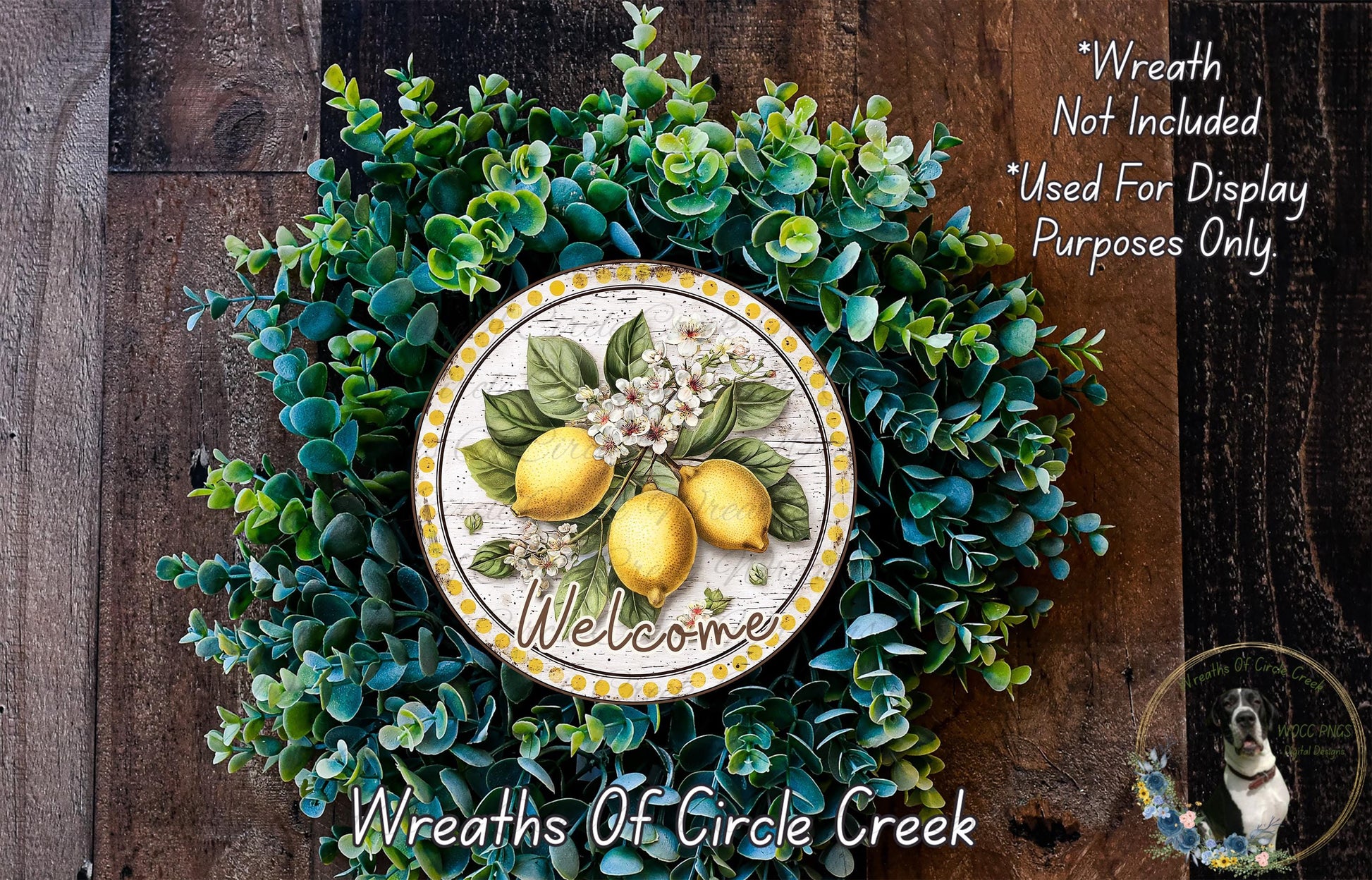 a wreath with a decorative plate in the center, surrounded by various green plants and flowers. The plate has a welcoming message written on it, and the wreath is displayed on a wooden surface.
