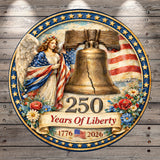The image is a decorative plaque celebrating the 250th anniversary of the United States' independence. It features a bell, an angel, and flowers, along with the text "250 Years Of Liberty 1776 2026".