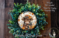A wreath made of green leaves and a cow wearing a hat, with the text "Hello Fall" written on it.