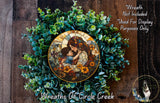 a wreath with a stained glass-style depiction of a woman holding a child, surrounded by green foliage. The wreath is placed on a wooden surface, and there is a small dog visible in the bottom right corner of the image.