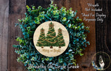 A wreath made of green plants and a circular wooden sign with a Christmas tree design, placed on a wooden surface.