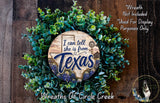 a wreath made of green leaves and a wooden sign with the text "I can tell she is from Texas" surrounded by a wooden background.