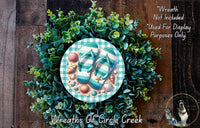A wreath made of green foliage and seashells, with a pair of flip flops placed on top of the wreath.