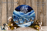 a round, blue-painted wreath with a winter village scene and a starry night sky. The wreath is surrounded by flowers and placed on a wooden surface.