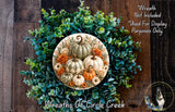 a wreath made of various fall-themed elements, including pumpkins, greenery, and flowers, set against a wooden background.