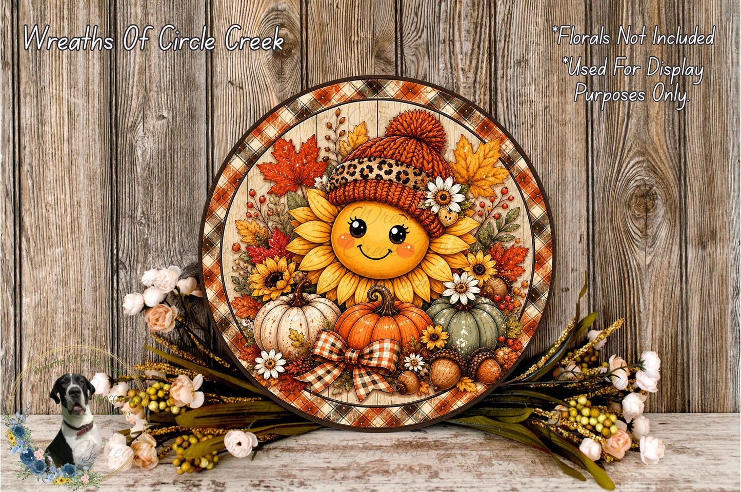 A decorative wreath with a smiling sunflower at the center, surrounded by autumn-themed elements such as pumpkins, leaves, and flowers, placed on a wooden surface.