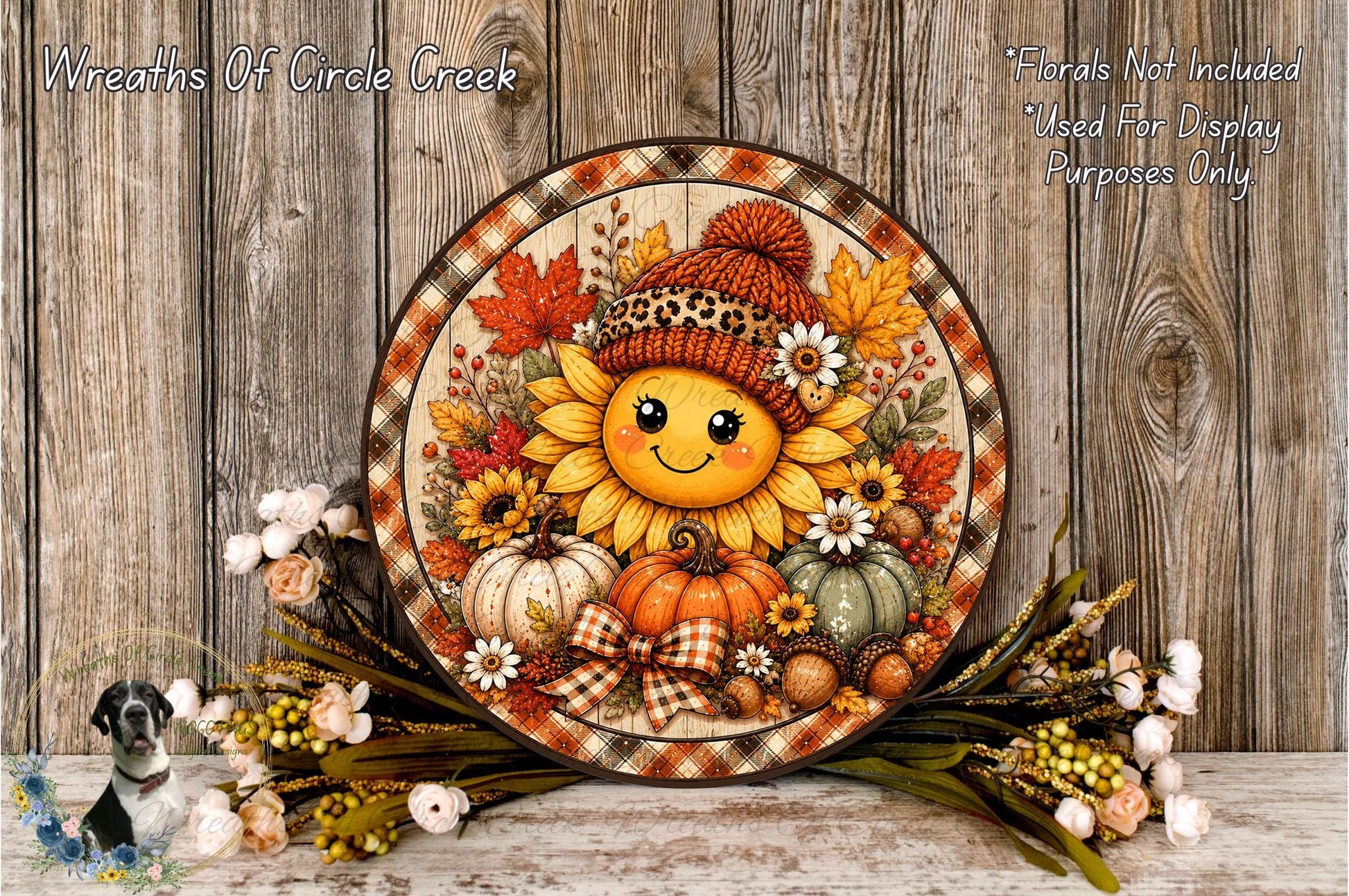A decorative wreath with a smiling sunflower at the center, surrounded by autumn-themed elements such as pumpkins, leaves, and flowers, placed on a wooden surface.