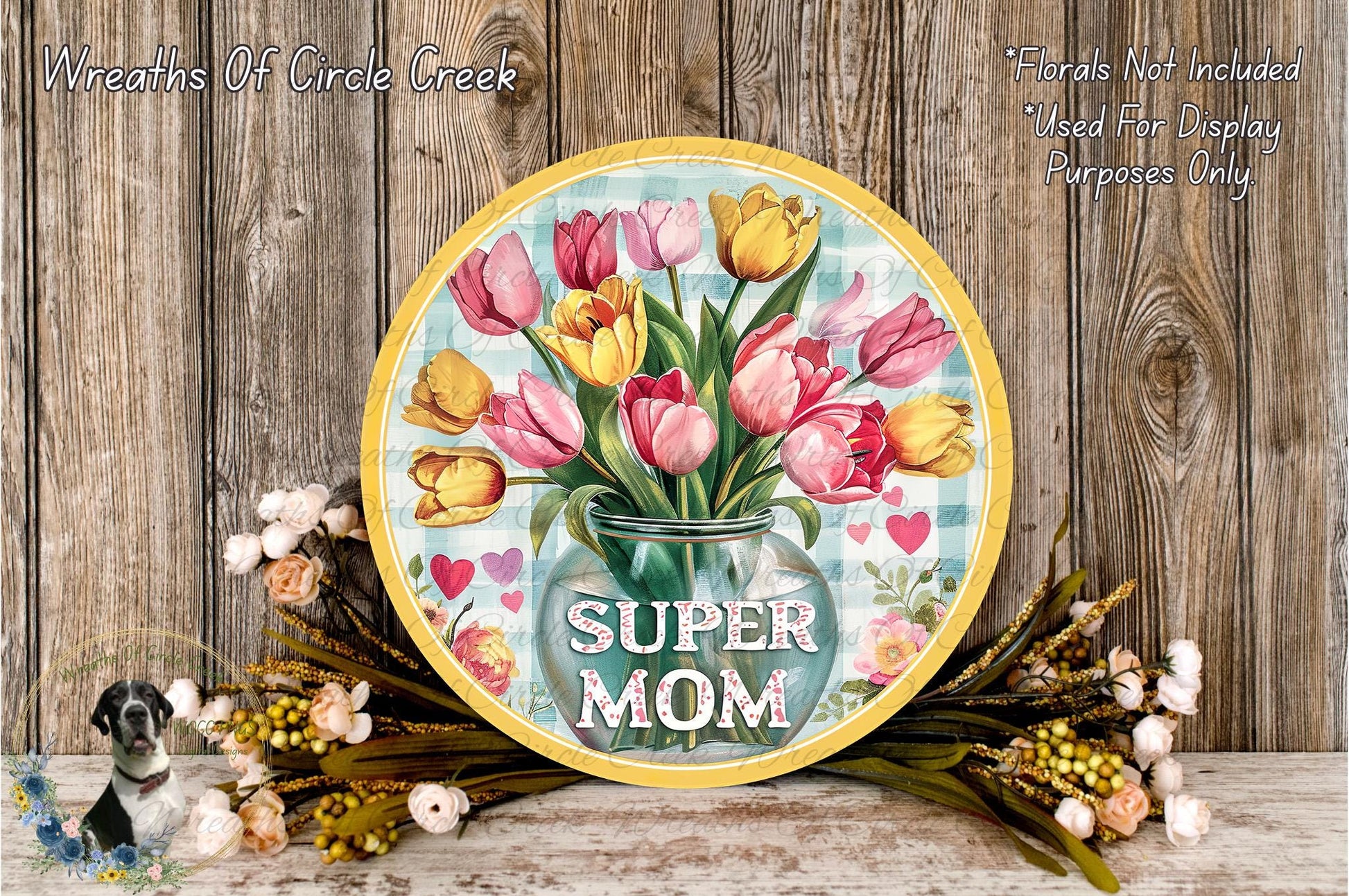 A round sign with a vase of colorful tulips and the text "SUPER MOM" displayed on it, surrounded by a floral arrangement and a wooden wall.