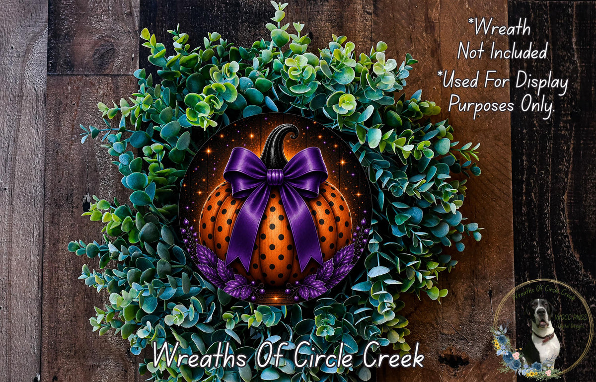 a wreath with a pumpkin and purple bow, surrounded by greenery, placed on a wooden surface.