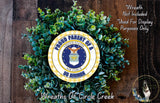 a wreath made of green leaves and a circular emblem with the text "Proud Parent of a US Airman" and the United States Air Force insignia.