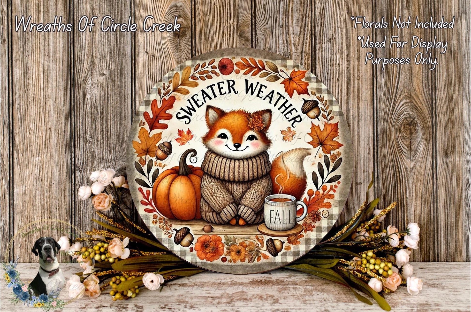 A decorative wreath featuring a fox wearing a sweater and surrounded by autumn-themed elements, including a pumpkin, flowers, and a mug of coffee.