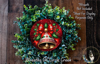 A festive Christmas wreath made of green leaves and red and gold ornaments, including a bell, is displayed on a wooden surface.