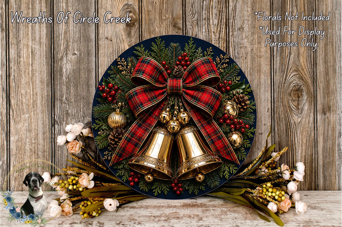 A festive Christmas wreath with a red and black plaid bow, bells, pine cones, and berries, displayed on a wooden surface.