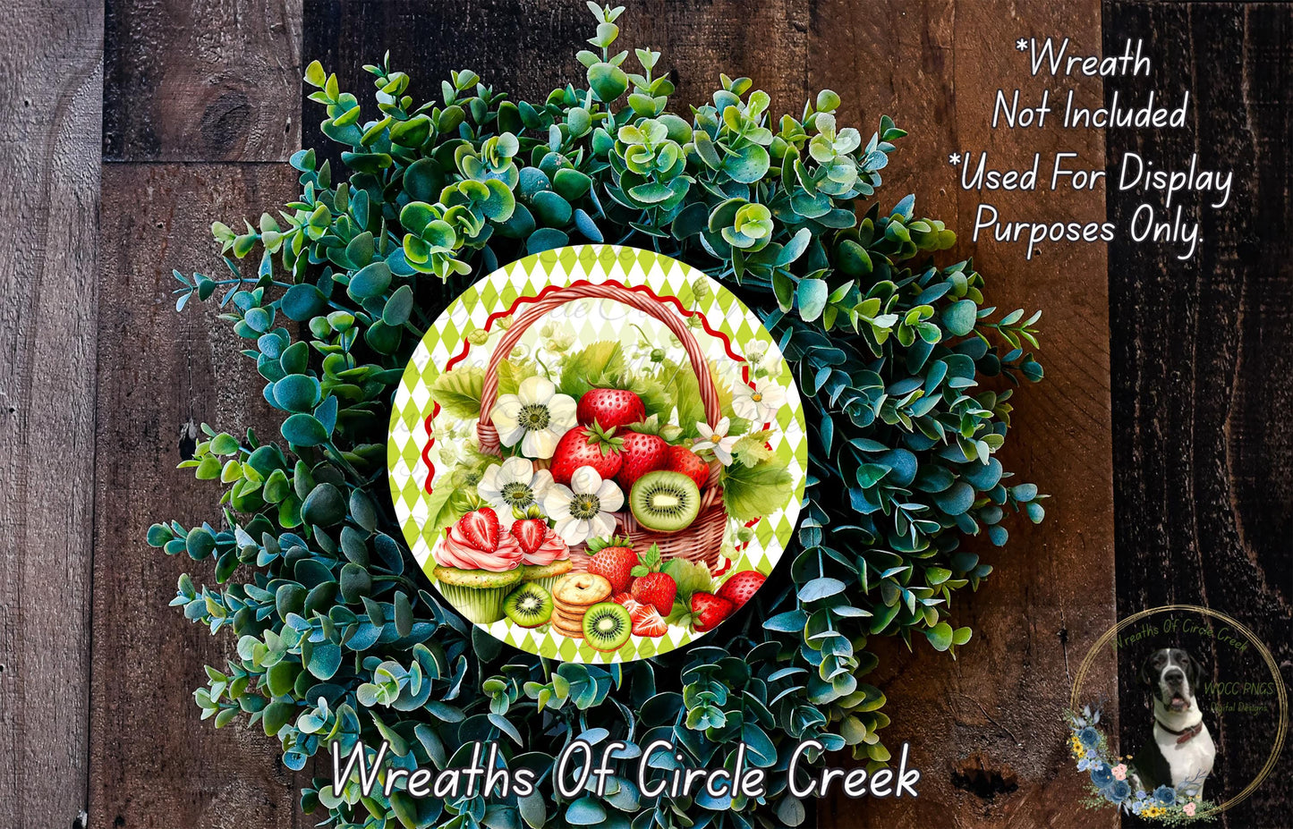 a wreath made of various green plants and flowers, including strawberries, kiwi, and other fruits and flowers. The wreath is displayed on a wooden surface, and there is a small dog visible in the bottom right corner of the image.
