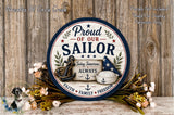 a round sign with the text "Proud of our Sailor" and an anchor, surrounded by flowers and a wooden background.