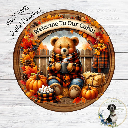 A wreath with a teddy bear holding a mug of coffee, surrounded by autumn leaves, pumpkins, and a dog. The wreath is framed by a wooden border, and the text "Welcome To Our Cabin" is displayed above the bear.