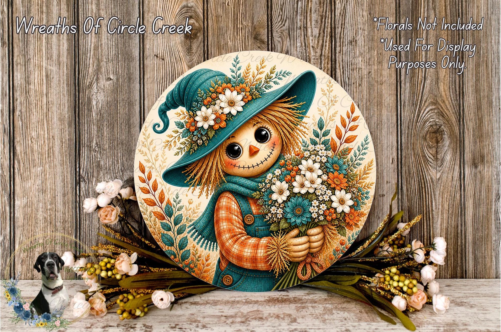 A round decorative plate featuring a scarecrow holding a bouquet of flowers, placed on a wooden surface with a wreath of flowers and greenery nearby.