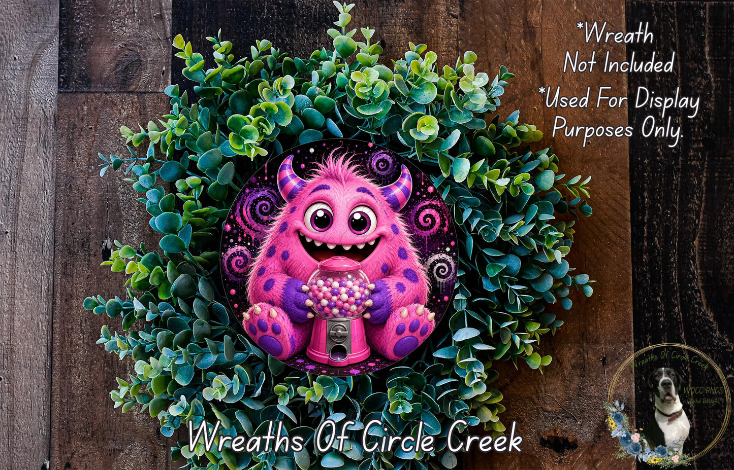 A whimsical wreath made of green foliage and featuring a large, colorful monster with horns and a pink body, holding a gumball machine.