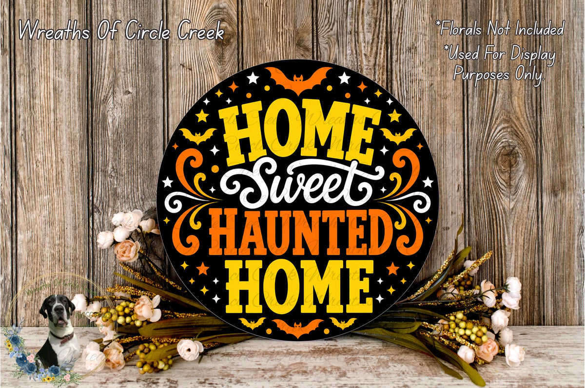 a decorative sign with the text "Home Sweet Haunted Home" displayed on a wooden surface. The sign is surrounded by a floral arrangement, creating a festive and spooky atmosphere.