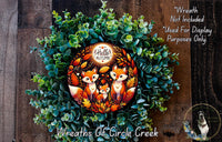 A wreath made of green leaves and flowers, featuring a central design of three foxes surrounded by autumn foliage. The wreath is displayed on a wooden surface, and there is a text overlay that reads "Wreath Not Included * Used For Display Purposes Only" and "Wreaths of Circle Creek".
