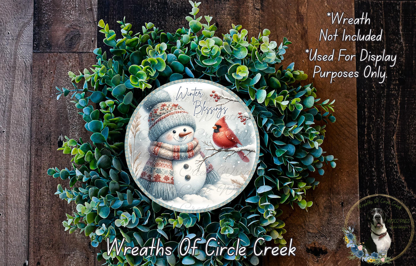 A wreath made of green leaves and a snowman, with a red cardinal perched on a branch. The snowman is wearing a scarf and a hat, and the snowman is holding a red cardinal. The wreath is displayed on a wooden surface, and there is text indicating that the wreath is not included in the display and is used for display purposes only.