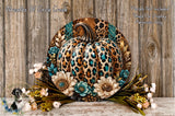 A decorative wreath featuring a leopard print pumpkin surrounded by flowers and foliage, placed on a wooden surface.