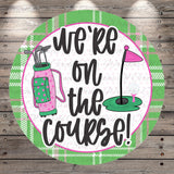 A circular sign with the text "we're on the course!" written on it, surrounded by golf-related elements such as a golf bag, clubs, and a golf ball.