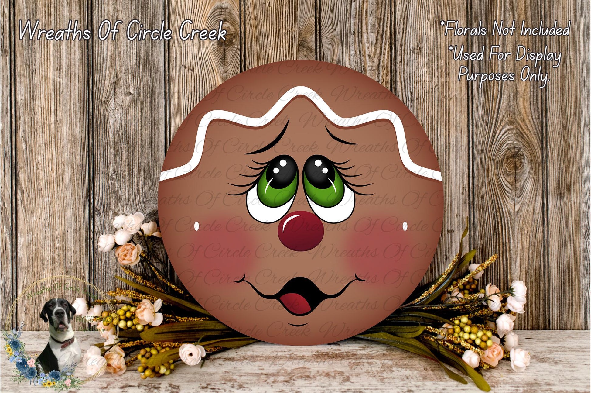 A gingerbread man-themed wreath with a face and eyes, placed on a wooden surface surrounded by flowers.