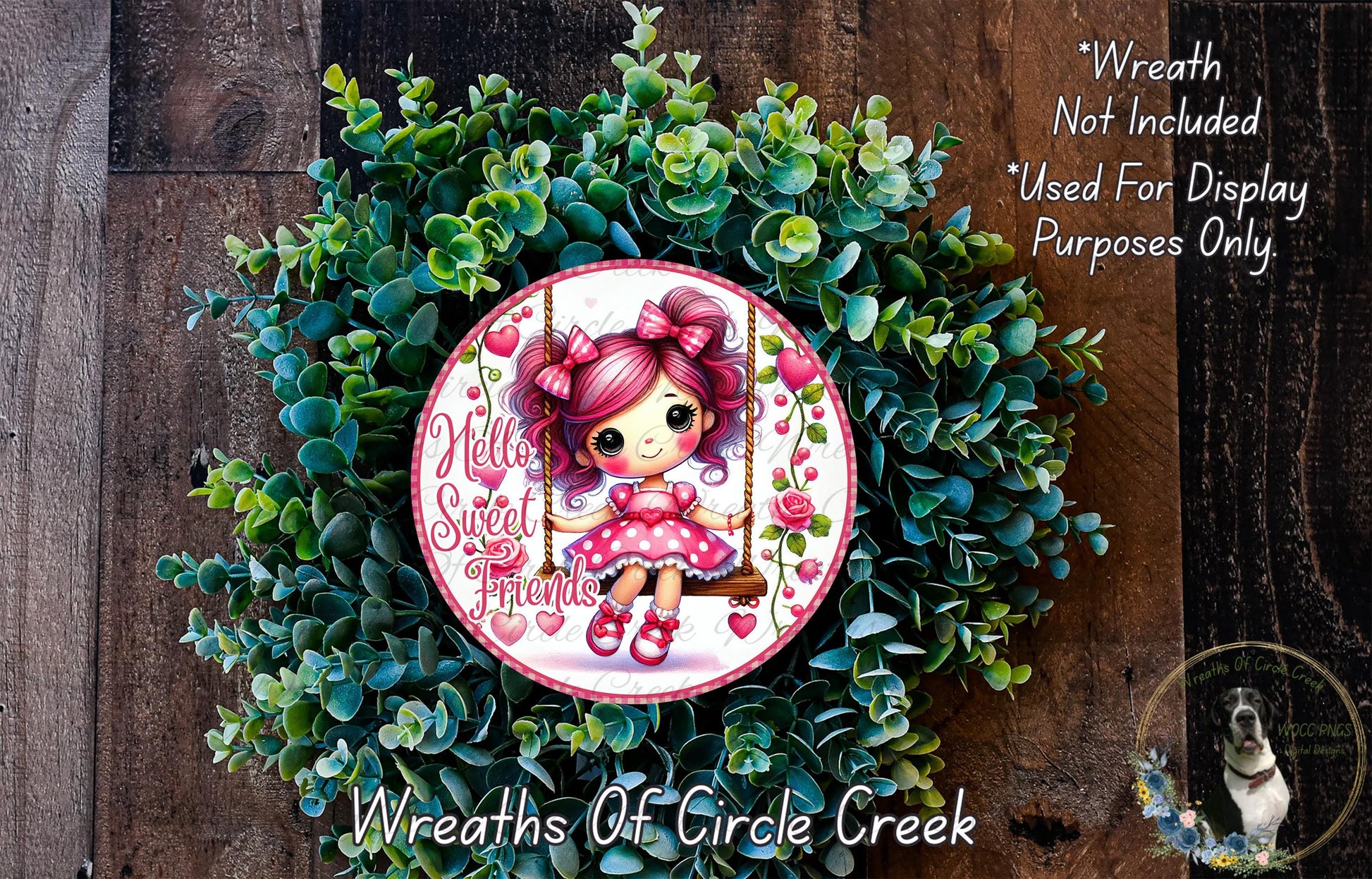 A wreath made of green leaves and flowers, featuring a small cartoon girl with pink hair and a pink dress. The wreath is displayed on a wooden surface, and there is a text overlay that reads "Wreath Not Included * Used For Display Purposes Only".