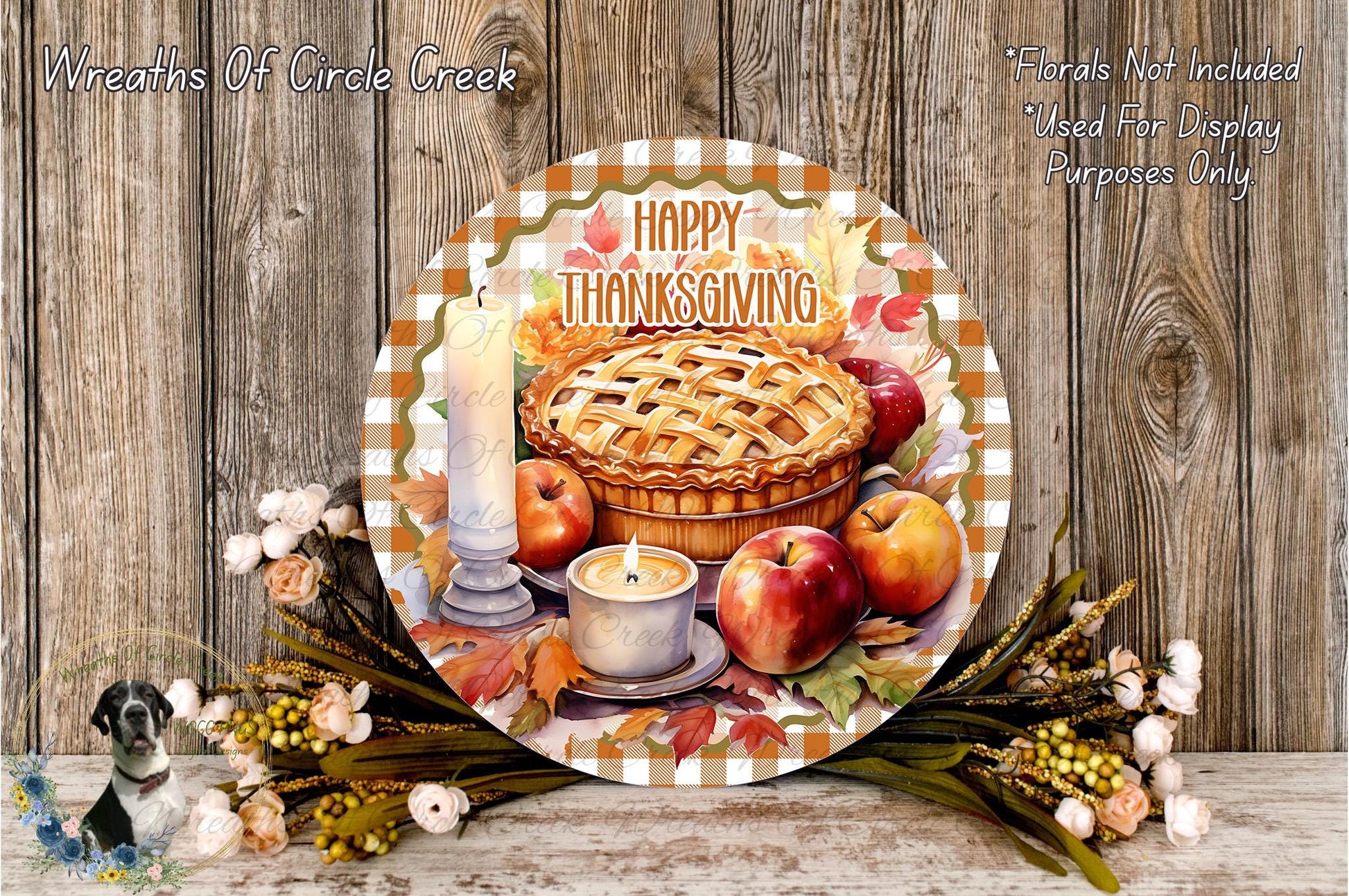 A decorative Thanksgiving wreath with a pie, apples, and flowers, along with a candle, is displayed on a wooden surface.