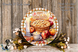 A decorative Thanksgiving wreath with a pie, apples, and flowers, along with a candle, is displayed on a wooden surface.