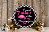 a decorative sign with a pink flamingo and the text "I just really like flamingos" against a black and white checkered background. The sign is surrounded by a floral arrangement and placed on a wooden surface.