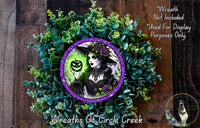 a wreath with a woman wearing a witch's hat and holding a pumpkin, surrounded by green foliage.