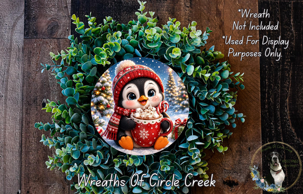 A wreath featuring a cute penguin wearing a red scarf and hat, holding a cup of hot chocolate, surrounded by green foliage.