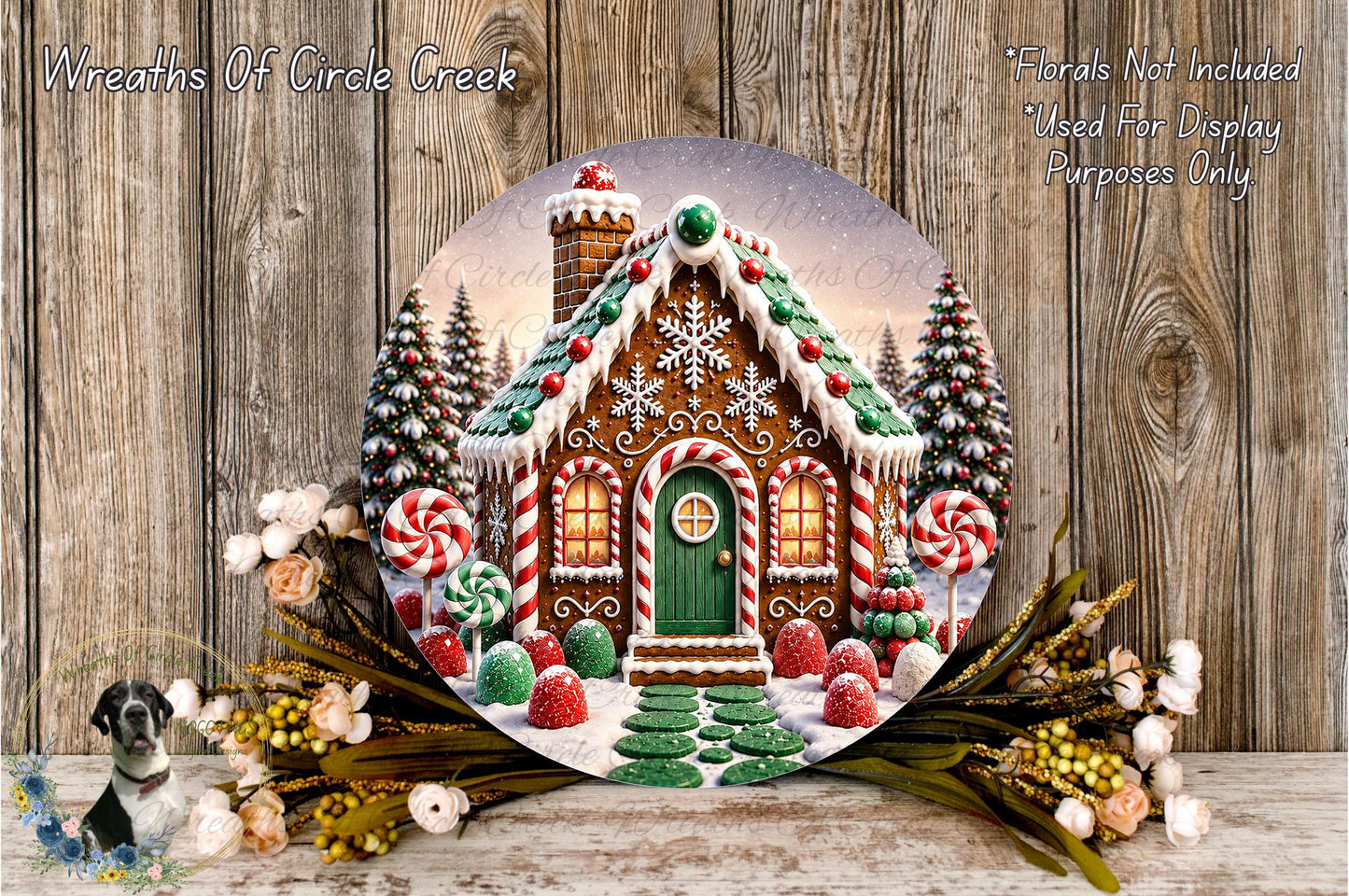 A round wooden plaque depicting a gingerbread house with a snowy landscape, surrounded by flowers and greenery.