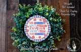 A wreath made of green leaves and flowers, with a circular sign in the center that says "She loves Jesus and America too".